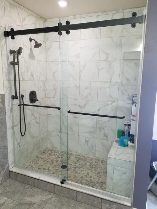Custom shower glass installation with frameless sliding shower door and black hardware for a modern bathroom